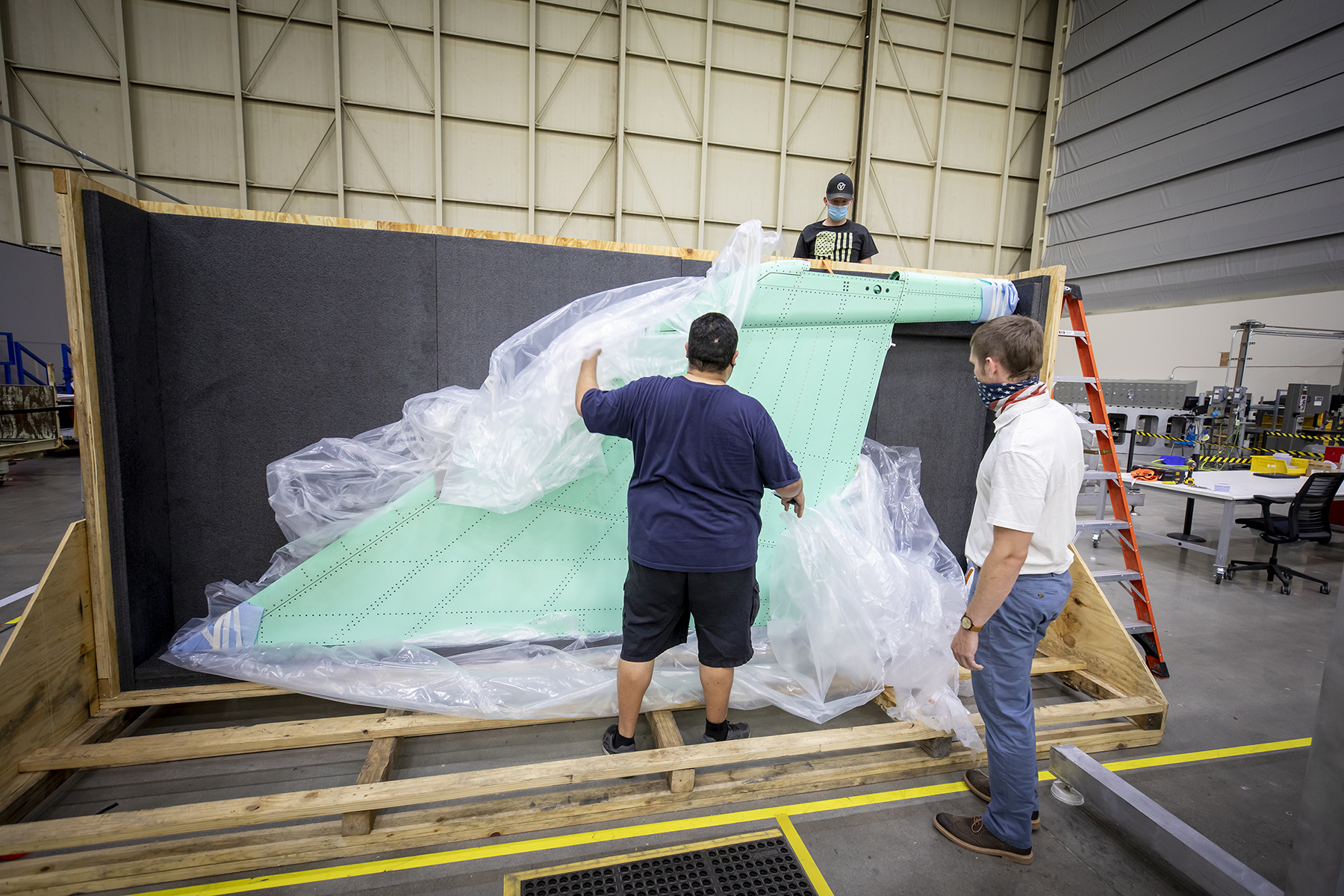 Three men unpacking the vertical stabilizer.