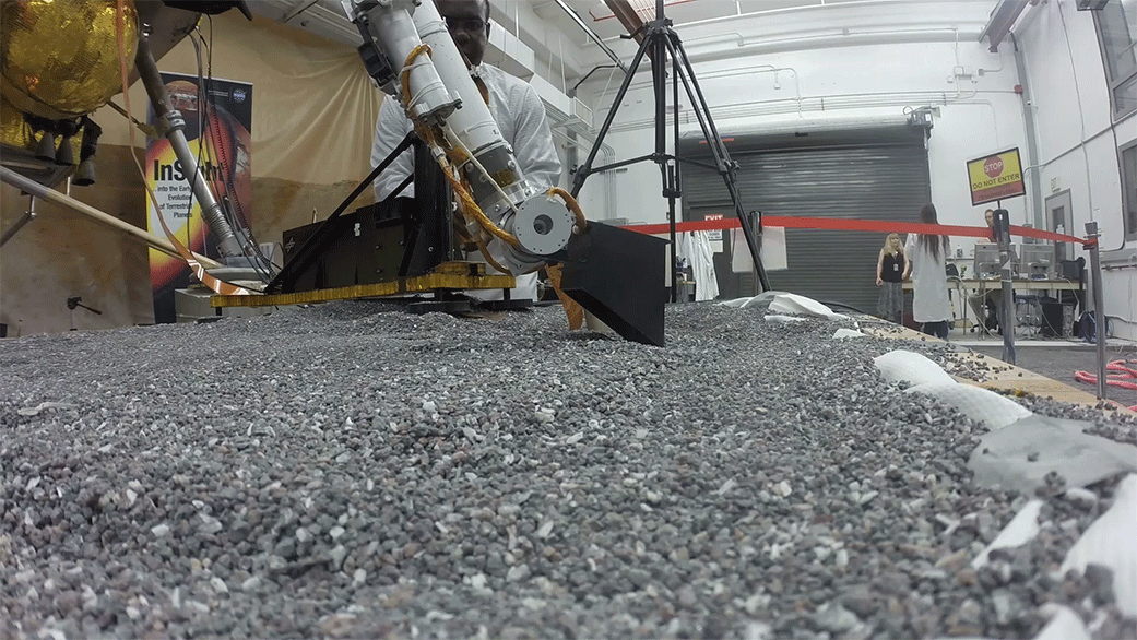A replica of InSight scraping soil with a scoop