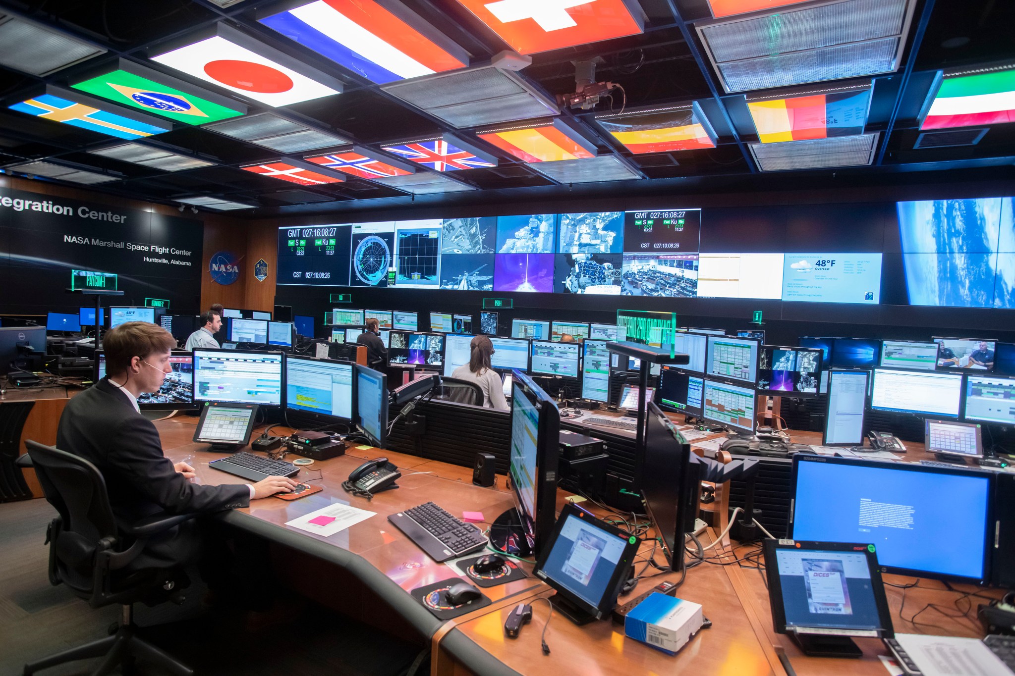 People sitting at computers with big screens on wall