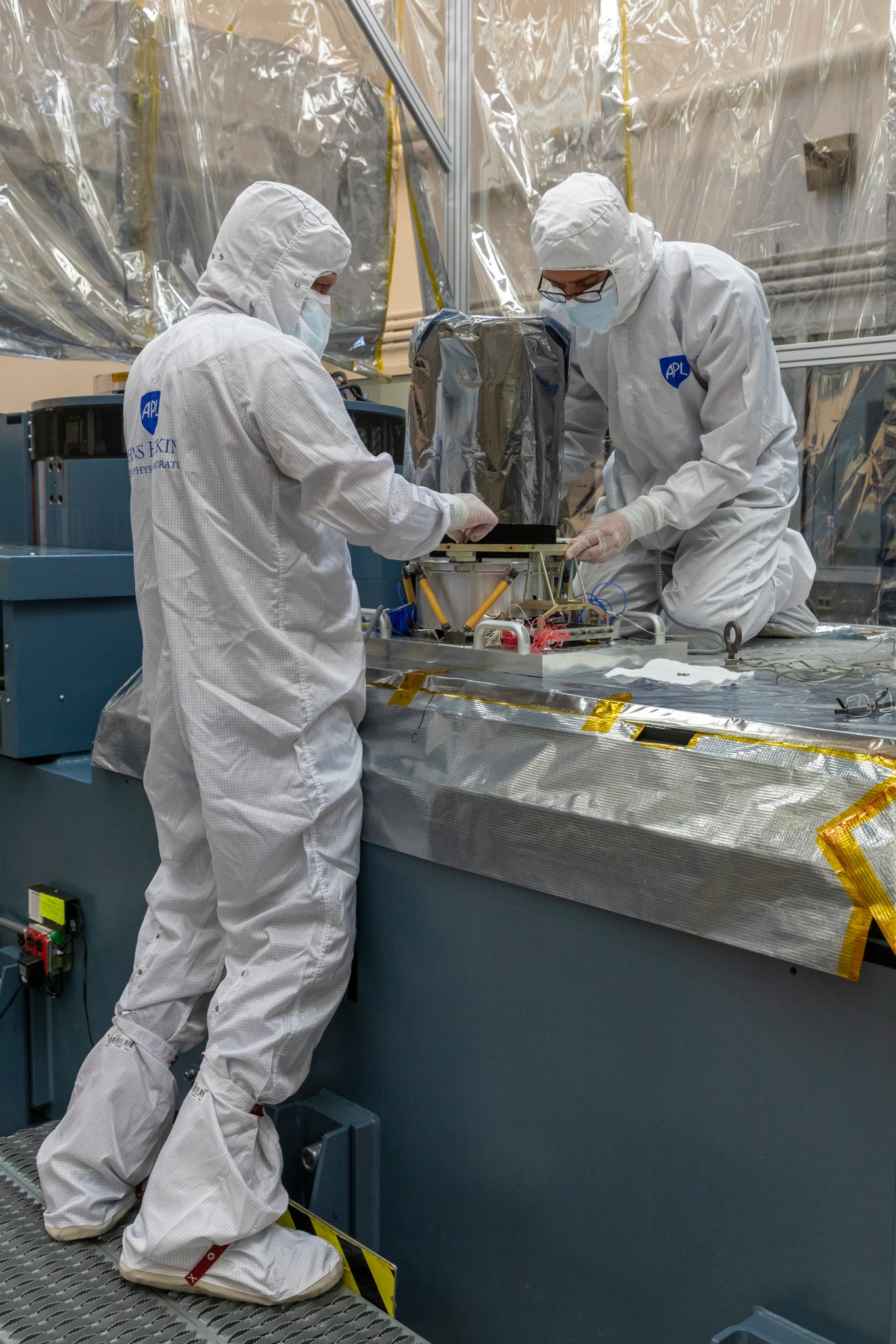 two people in protective suits work on a foil-covered instrument box