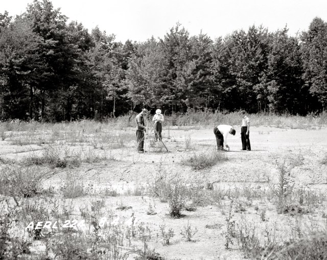 Black and white image of surveyors on an open field.