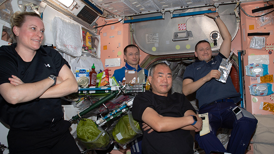 Four Expedition 64 crew members are pictured relaxing after a meal at the end of the work day inside the Unity module.