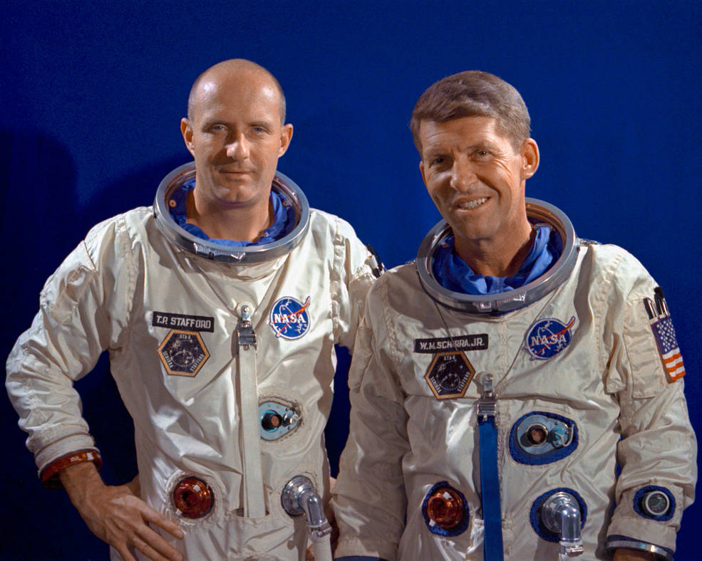 Astronauts Thomas Stafford and Walter Schirra in white spacesuits with black background