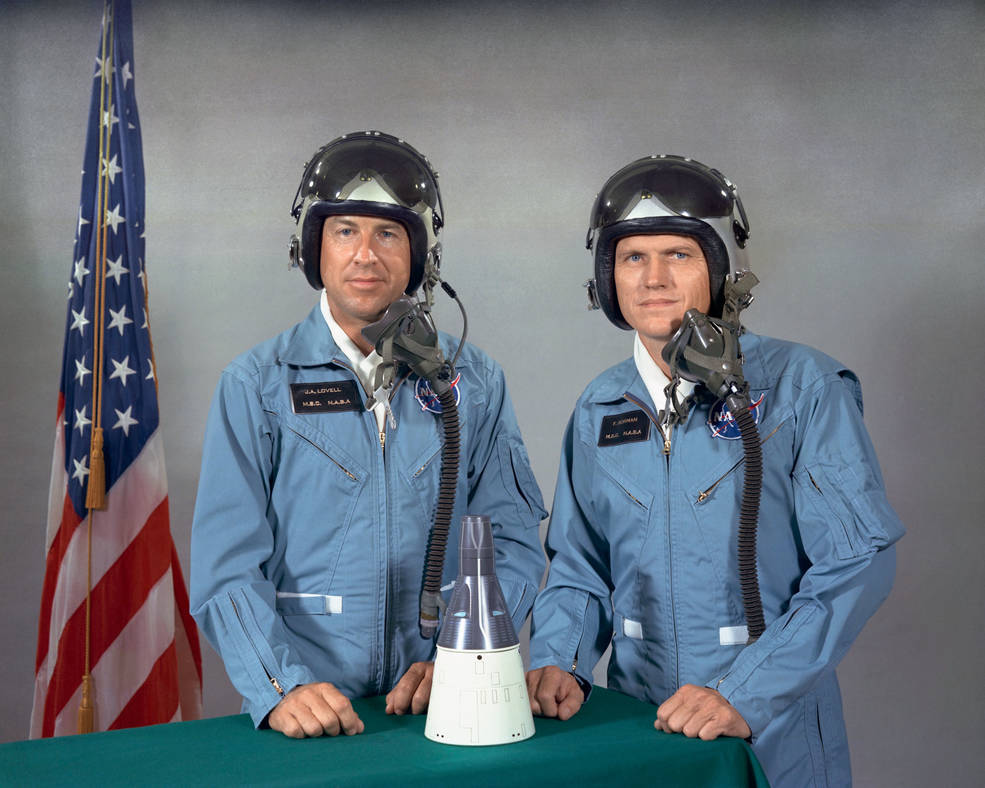 James Lovell and Frank Borman pose for crew photo with model ship in front of flag