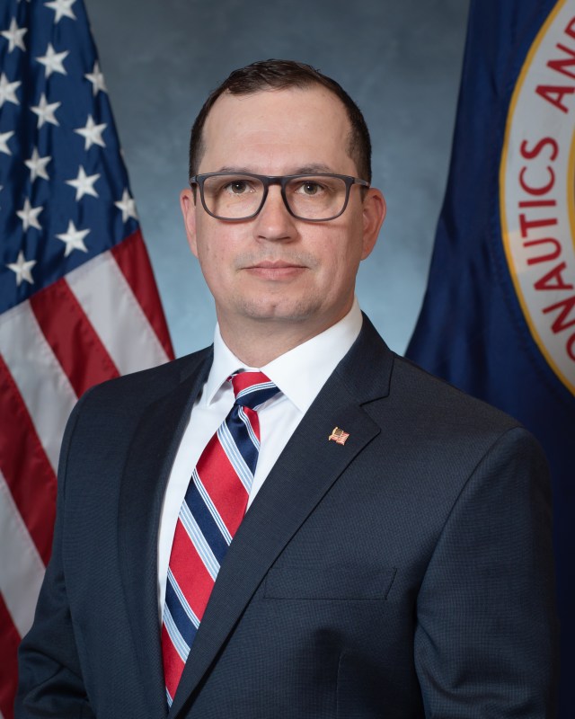 Portrait of Steven Dykeman with U.S. and NASA Flags in background.