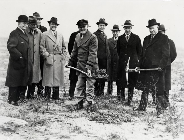 Several men in 1941 stand in an empty field. Two have shovels full of soil for a groundbreaking ceremony