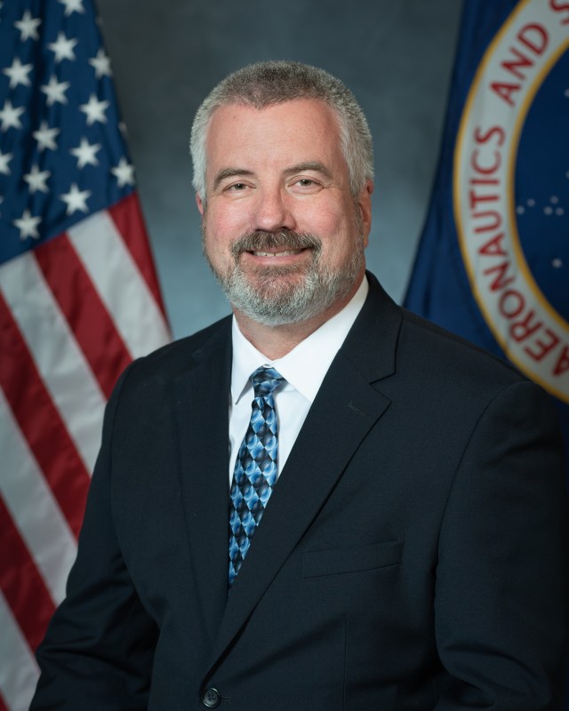 Portrait of John Hamley with U.S. and NASA Flags in background.