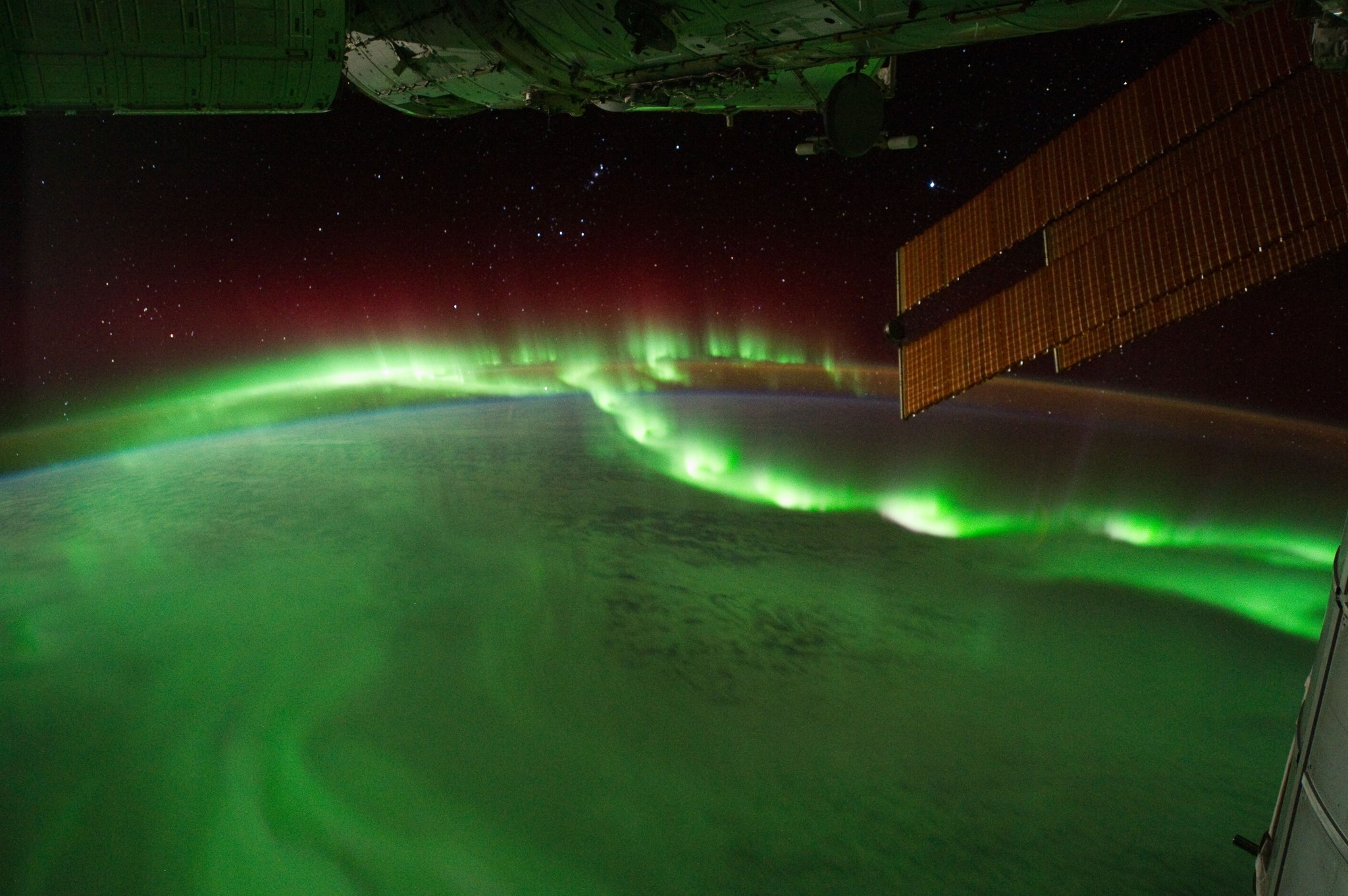 glowing, green-hued aurora, seen above surface of Earth from ISS, with solar array in partial view