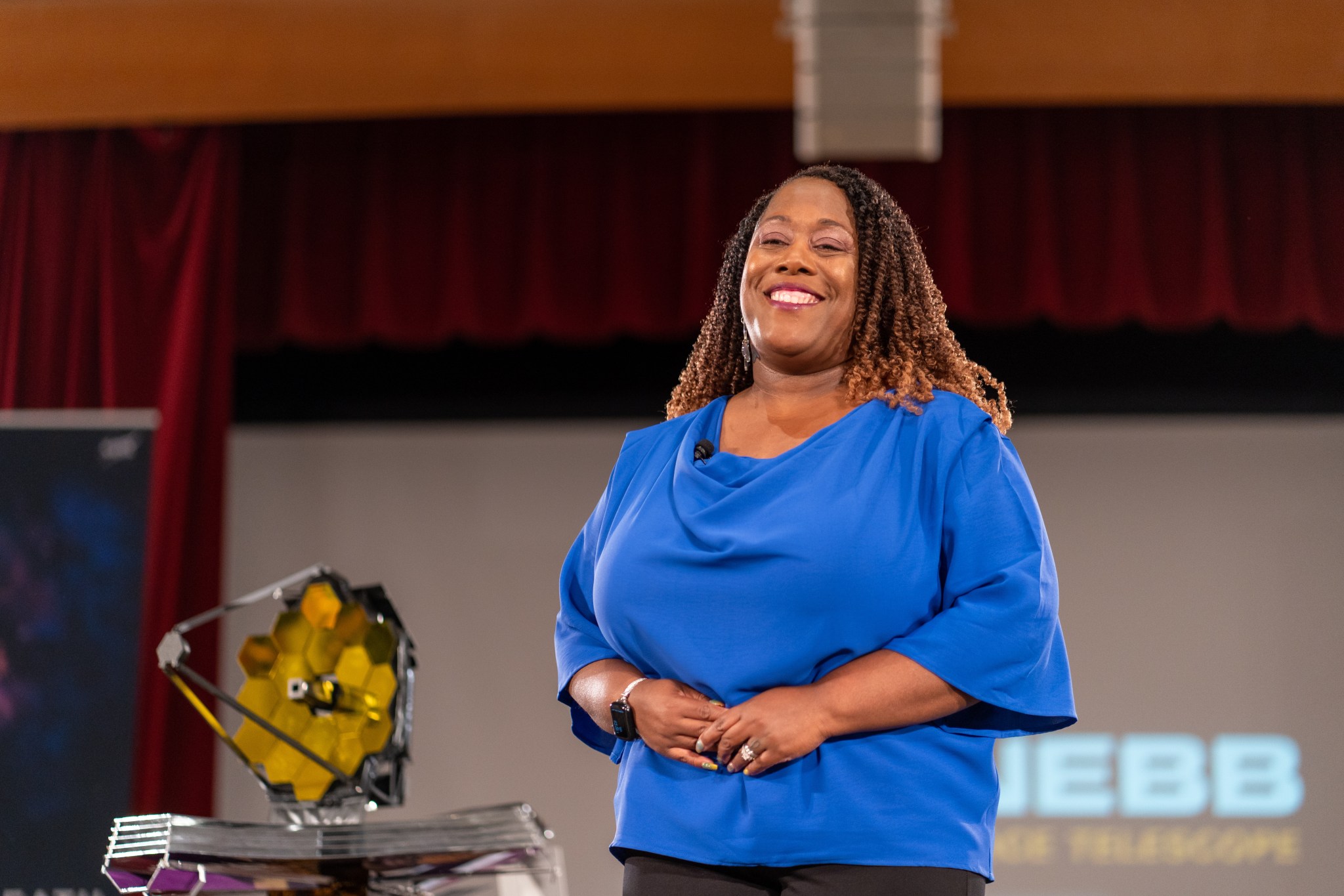 Michelle Jones stands on stage with a small model of the Webb Space Telescope to her right.