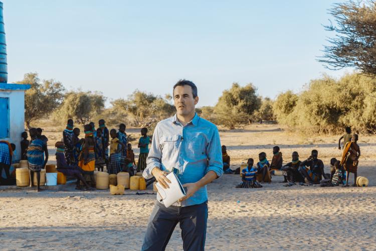 Photo of white man in blue shirt in front of black people waiting for water
