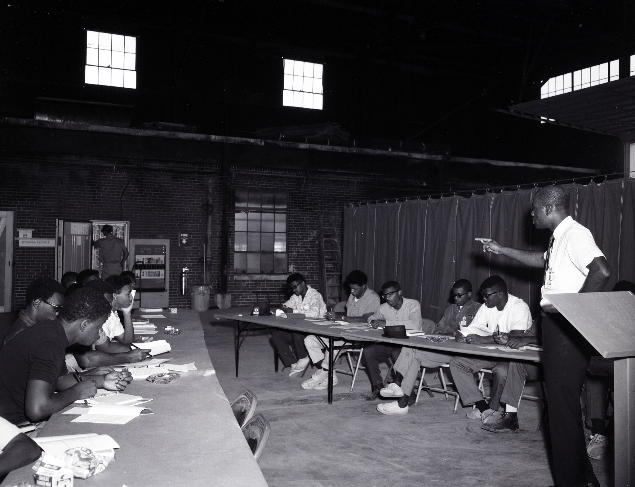 An instructor talks to students sitting at tables with their notes.