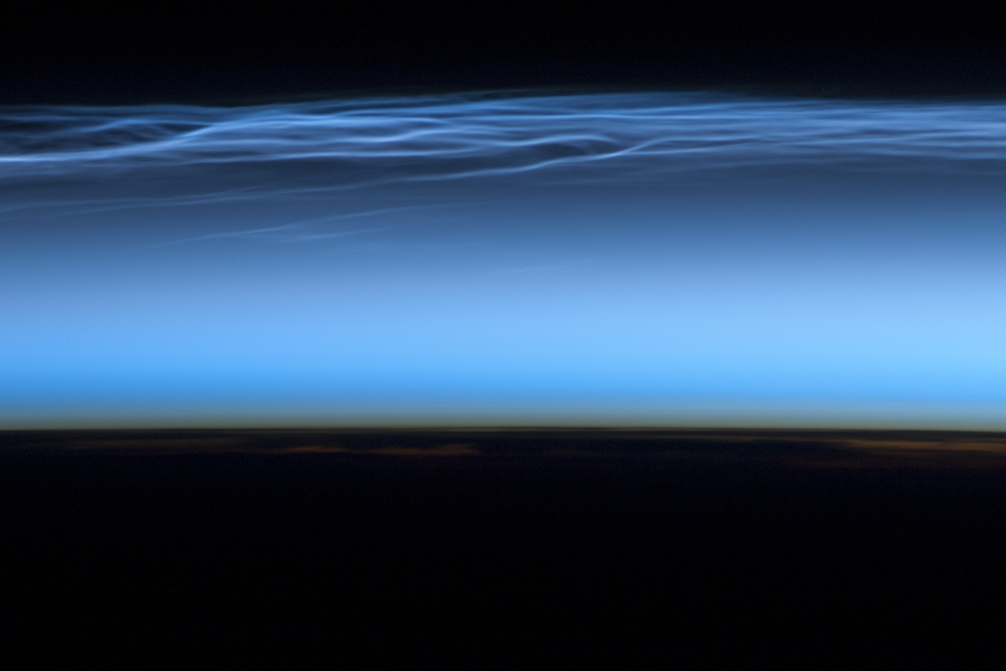 Blue haze appears above a dark horizon. Near the top of the blue haze appear thin, blue, wavy clouds.