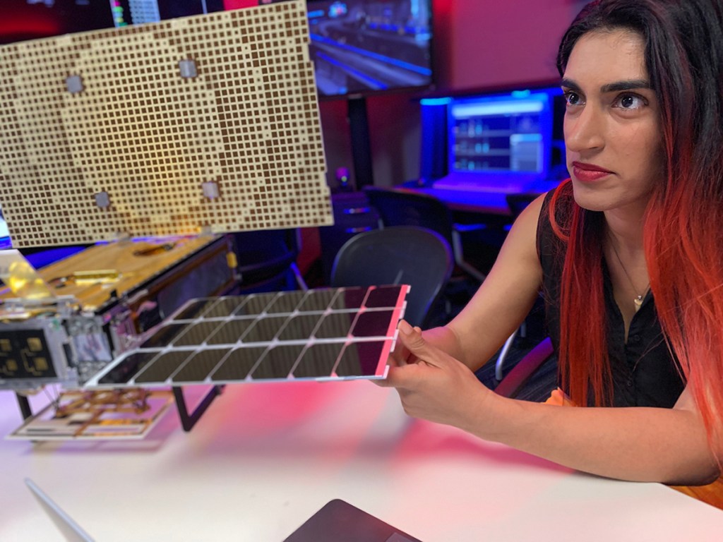 Systems Engineer Farah Alibary sitting next to space hardware