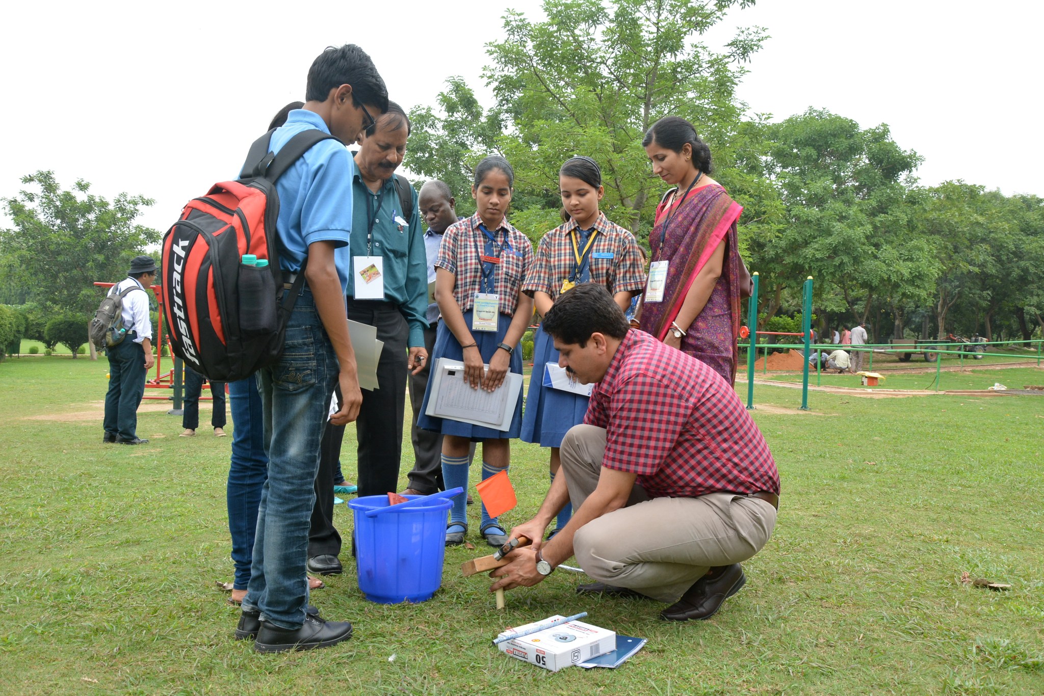 Student and teachers gather areound a measurement bucket in a field.