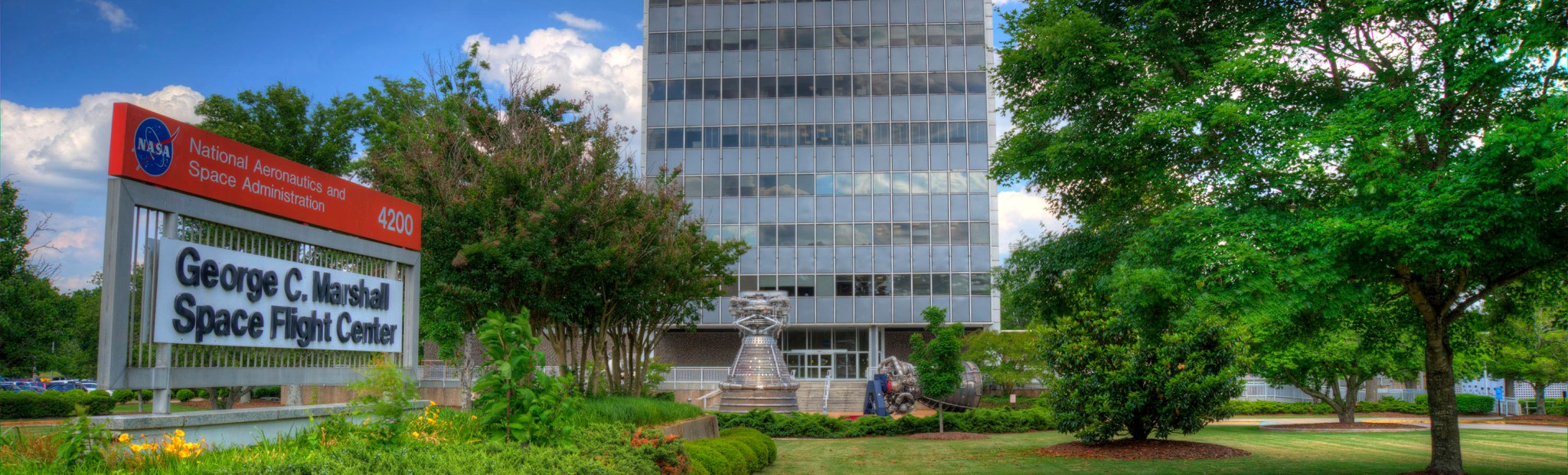 Thumbnail of a sign at NASA's Marshall Space Flight Center and a tall building behind it.