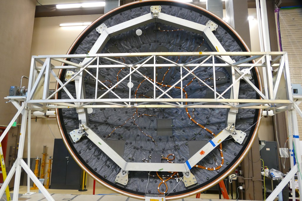 MEDLI2 sensors, electronics, and harnessing installed on the inner surface of the Mars 2020 heat shield while it is mounted on the heat shield turn-over fixture. The MEDLI2 harness has a circuitous routing to avoid the wheels of the Perseverance rover.