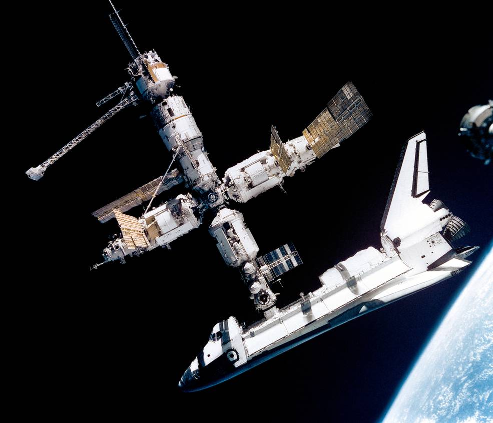 View of the Mir space station with Space Shuttle Atlantis attached. In the background is the blackness of space with a portion of the Earth visible in the lower left-hand corner.