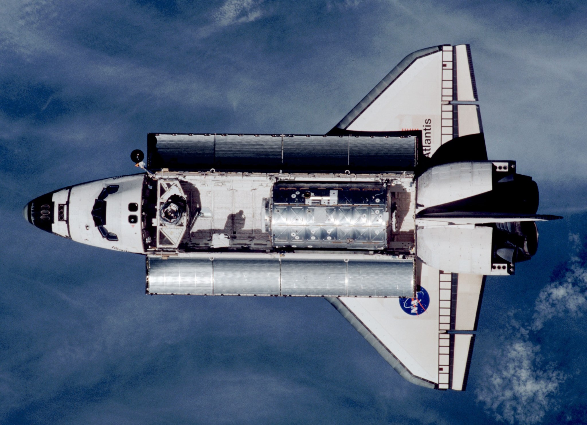 An aerial view of Space Shuttle Atlantis with the Earth's atmosphere below.