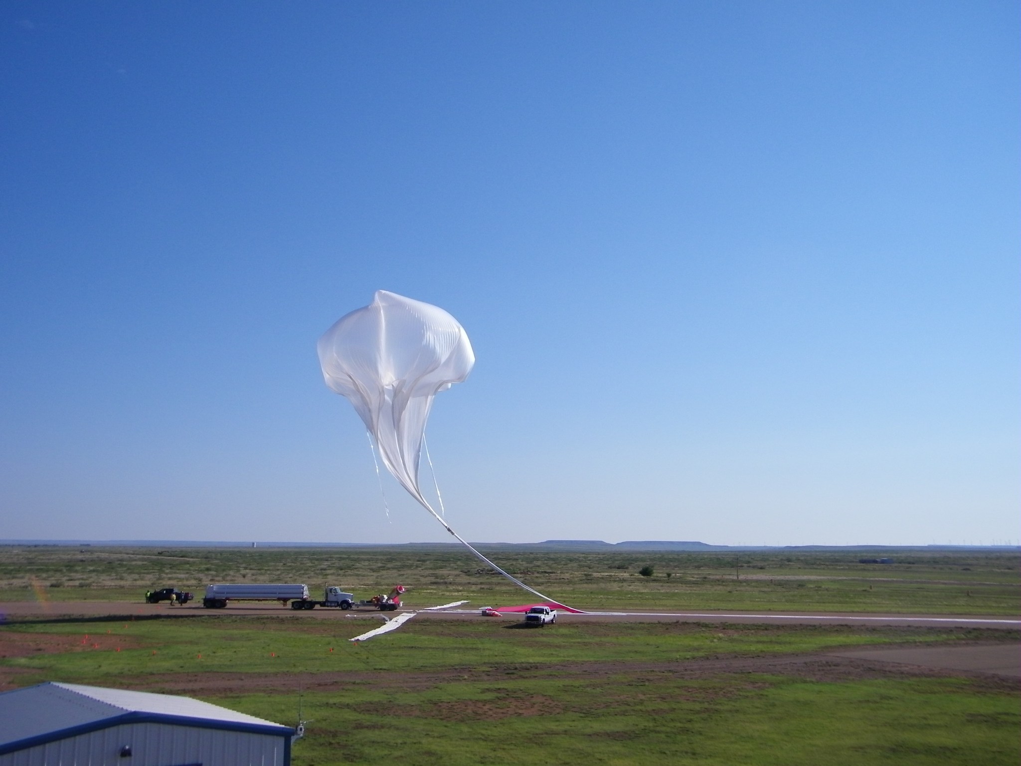 A scientific balloon partially inflated preparing to launch against a blue sky.
