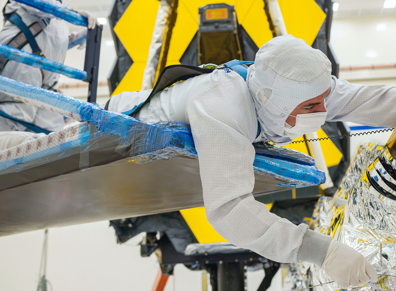 A technician carefully works on folding the sunshield of The James Webb Space Telescope.
