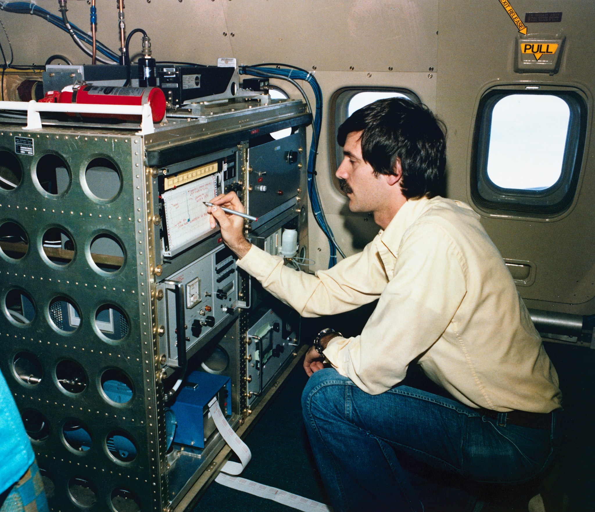 A research scientists writes data readings on an equipment rack aboard a researcher aircraft .