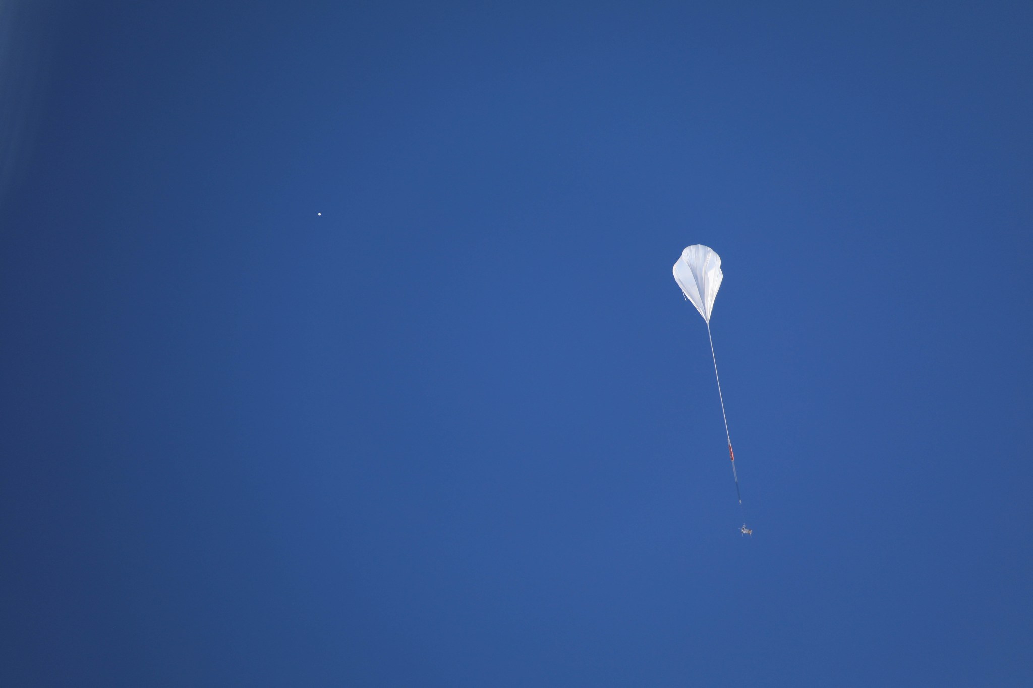 Scientific ballon lifting off against blue sky.