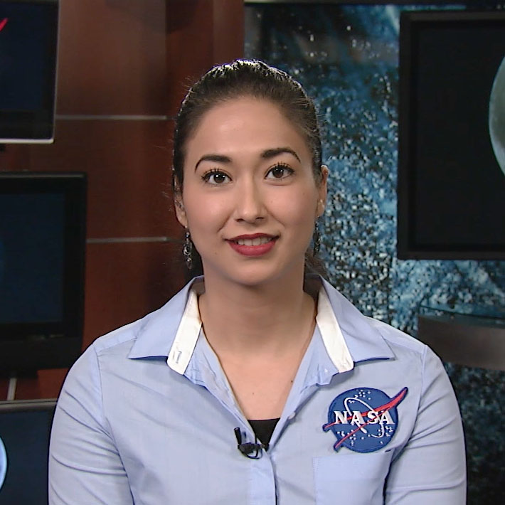 Portrait of Nayi Castro looking at the camera with a soft smile. She is wearing a blue collared shirt with a NASA patch.