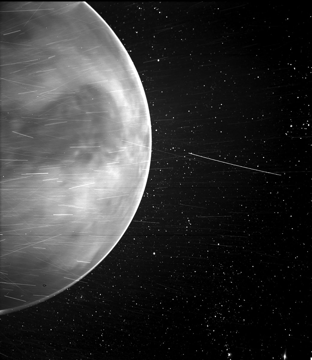 A black and white image showing one hemisphere of planet Venus against a backdrop of stars, with bright streaks throughout.