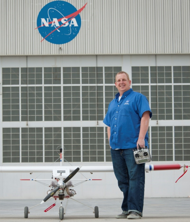 Robert "Red" Jensen stands next to a model airplane at a NASA facility
