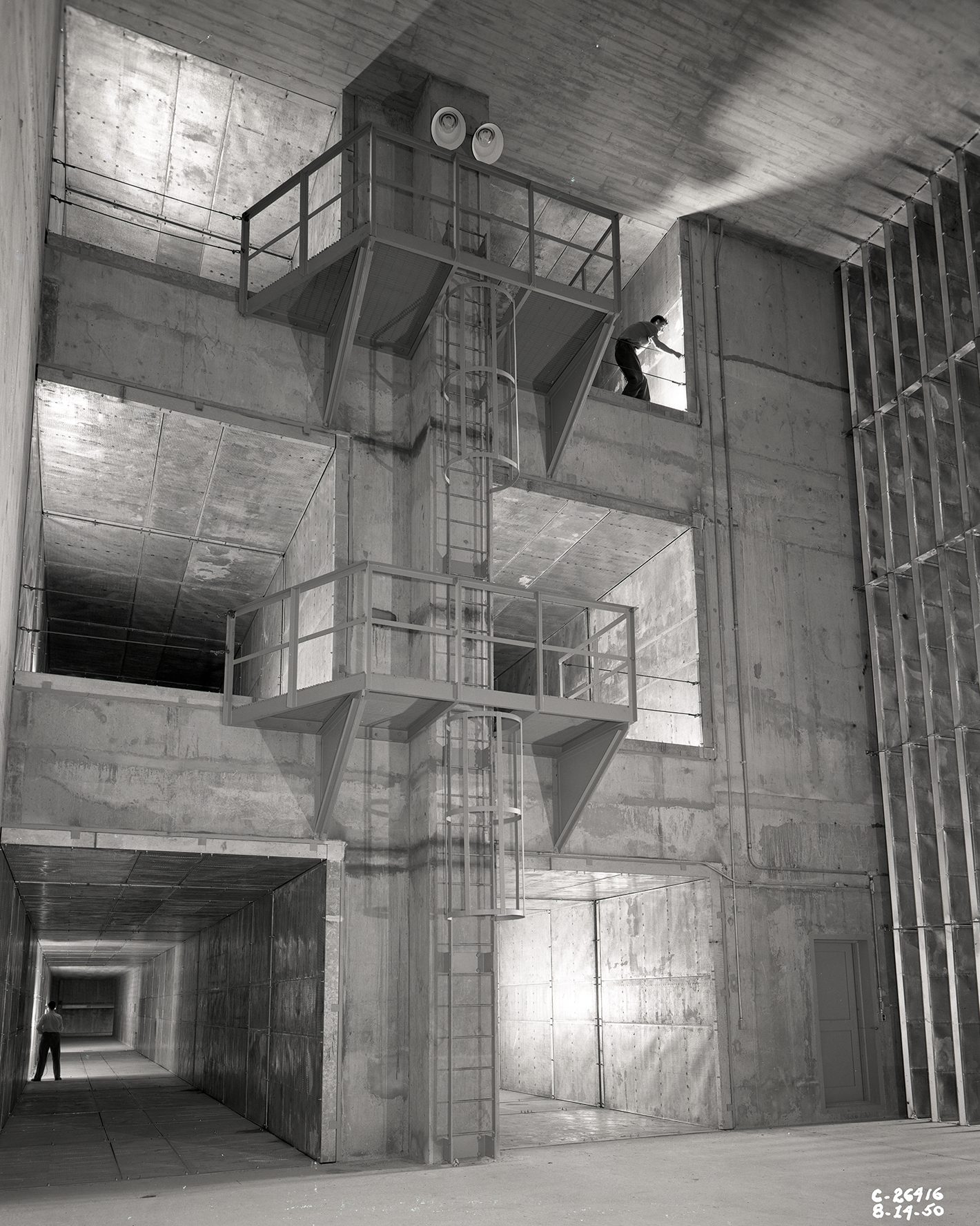 Workers stand inside wind tunnel openings at three vertical levels.