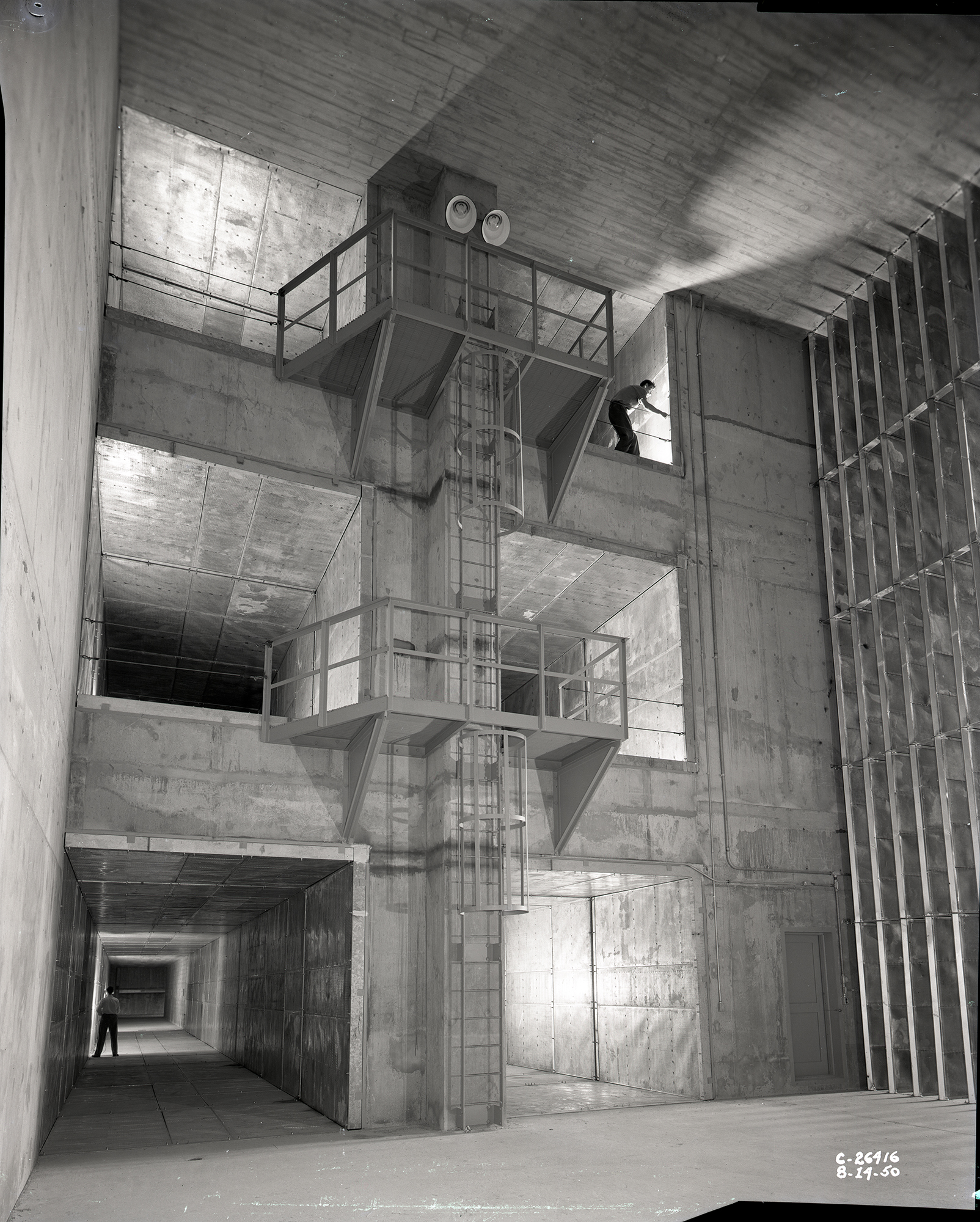 Workers stand inside wind tunnel openings at three vertical levels.