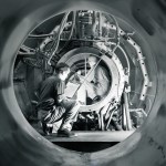Two engineers crouching with clipboards inside a circular propellant test facility.
