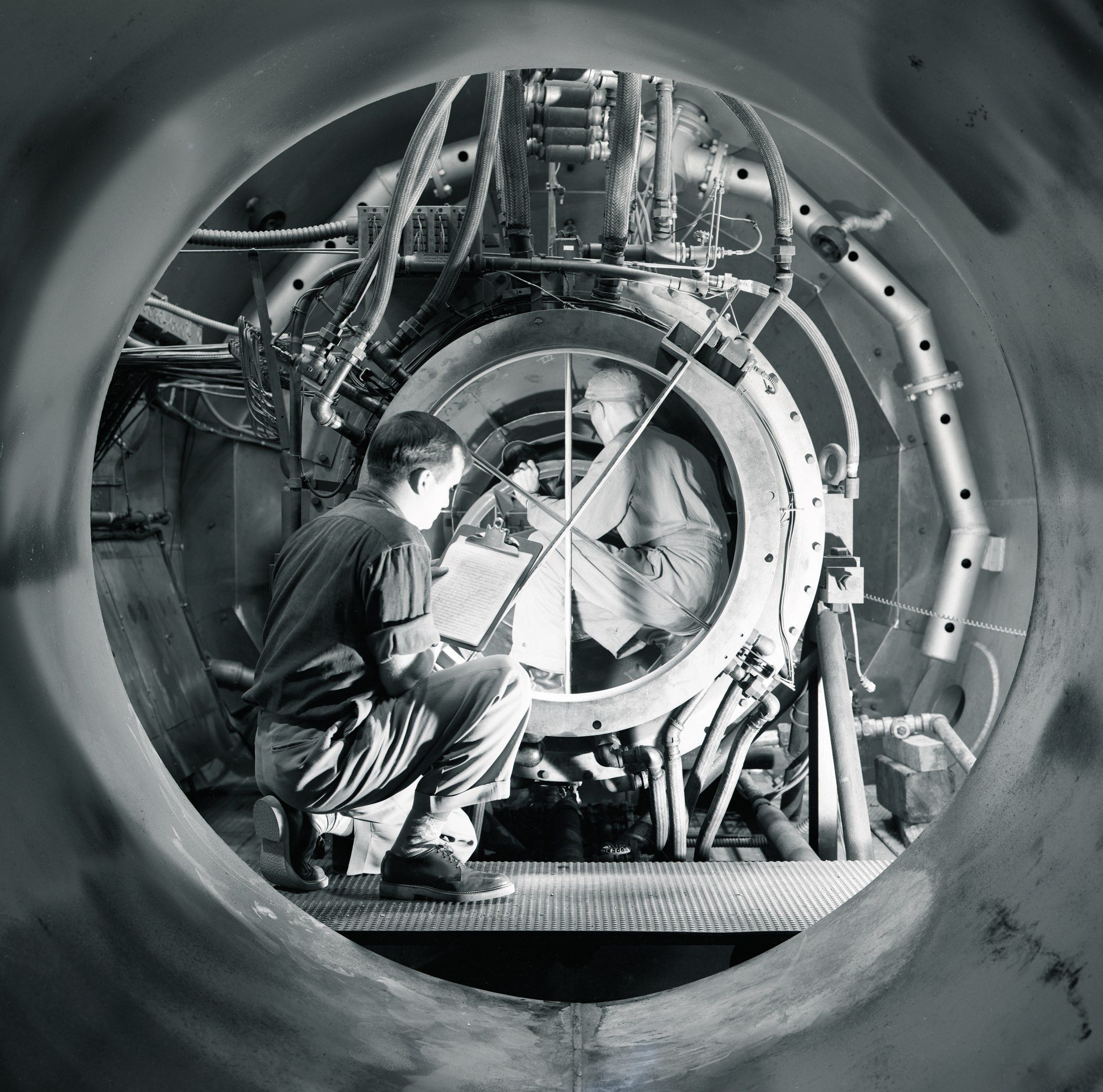 Two engineers crouching with clipboards inside a circular propellant test facility.