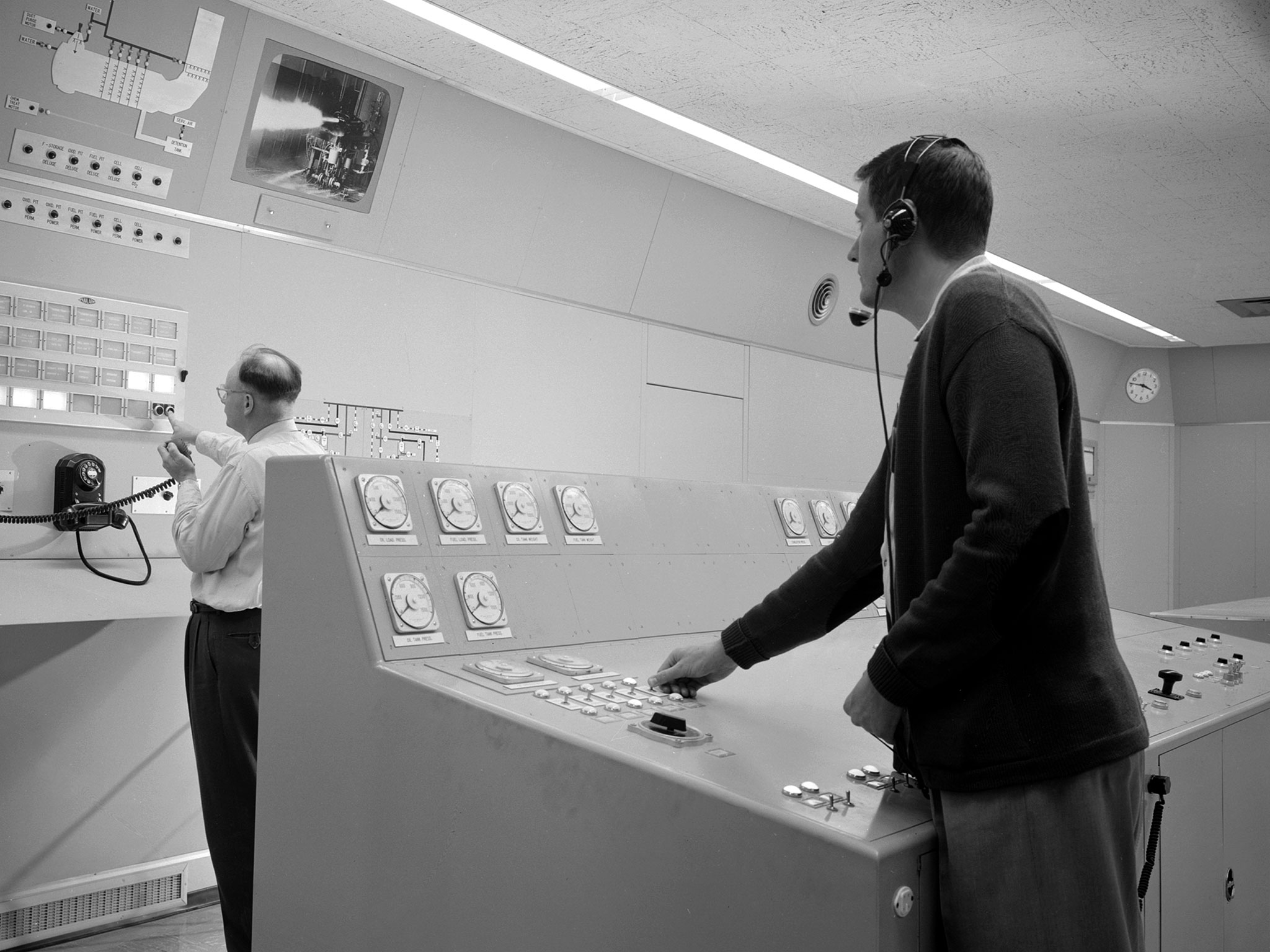 Two men in control room watching monitor.