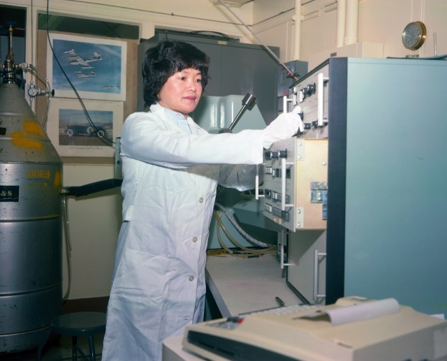 Asian-American woman in lab coat adjusting equipment.