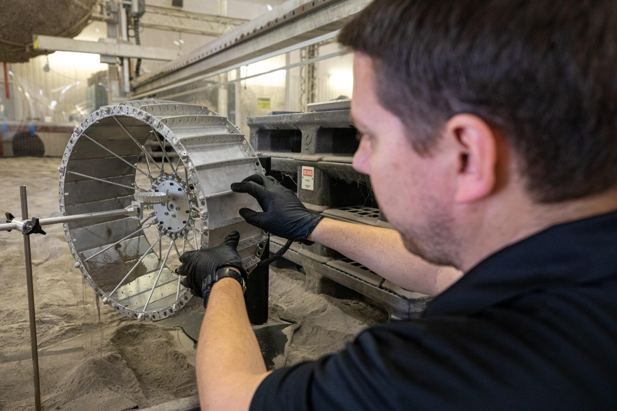 A man adjusts a wheel from NASA's Moon exploration rover, VIPER, in a test chamber containing simulated Moon dirt and dust.