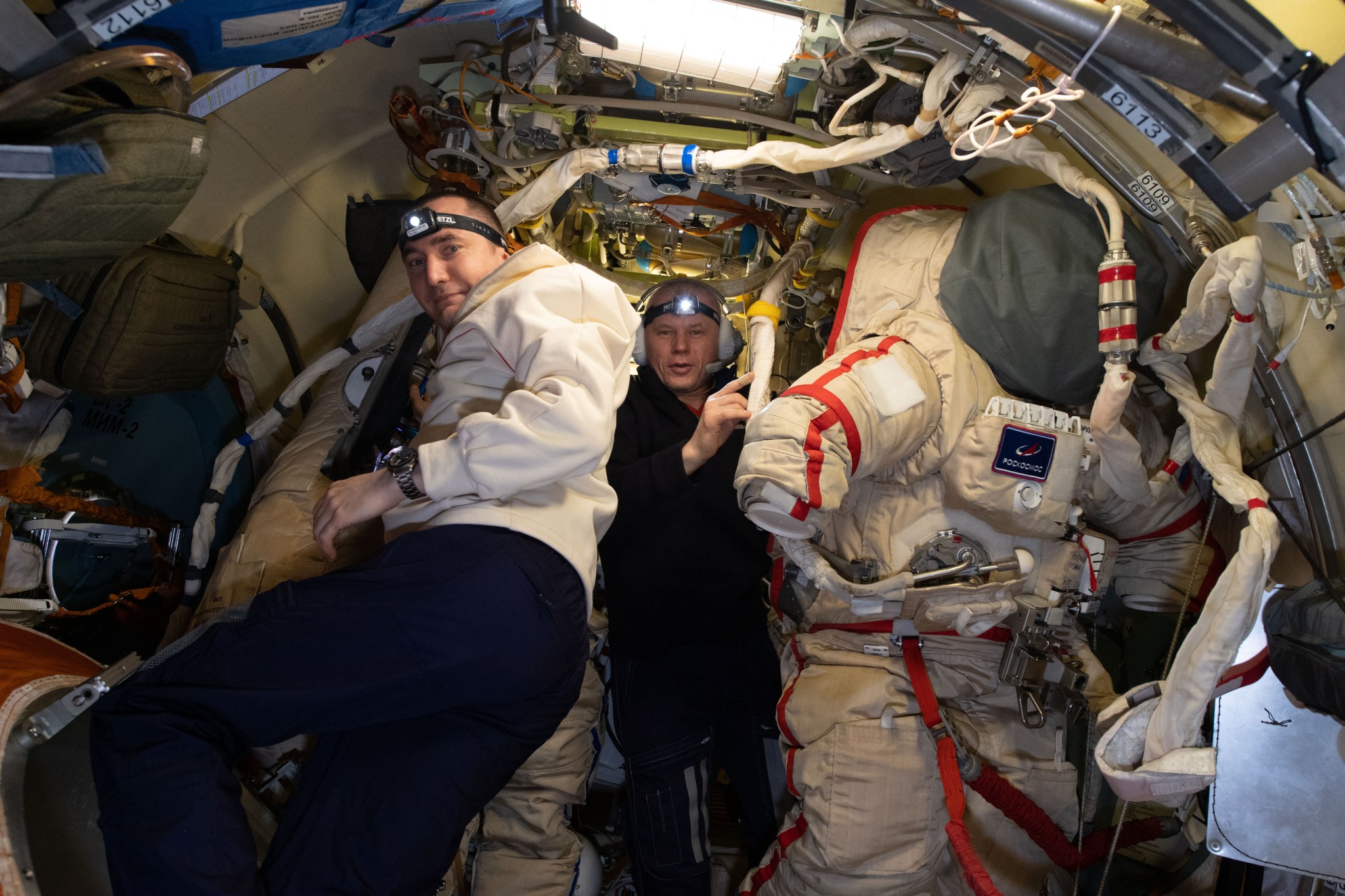 Roscosmos Flight Engineers Pyotr Dubrov, left, and Oleg Novitskiy prepare Russian Orlan spacesuits inside the International Space Station's Poisk mini-research module for an upcoming spacewalk.