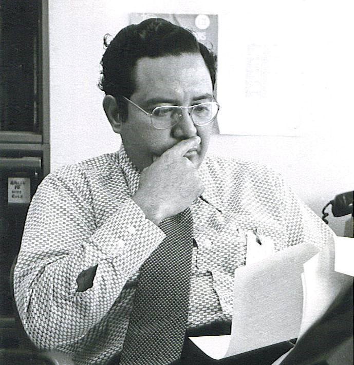 Arturo Campos sits in a chair, looking at a piece of paper in his hand.