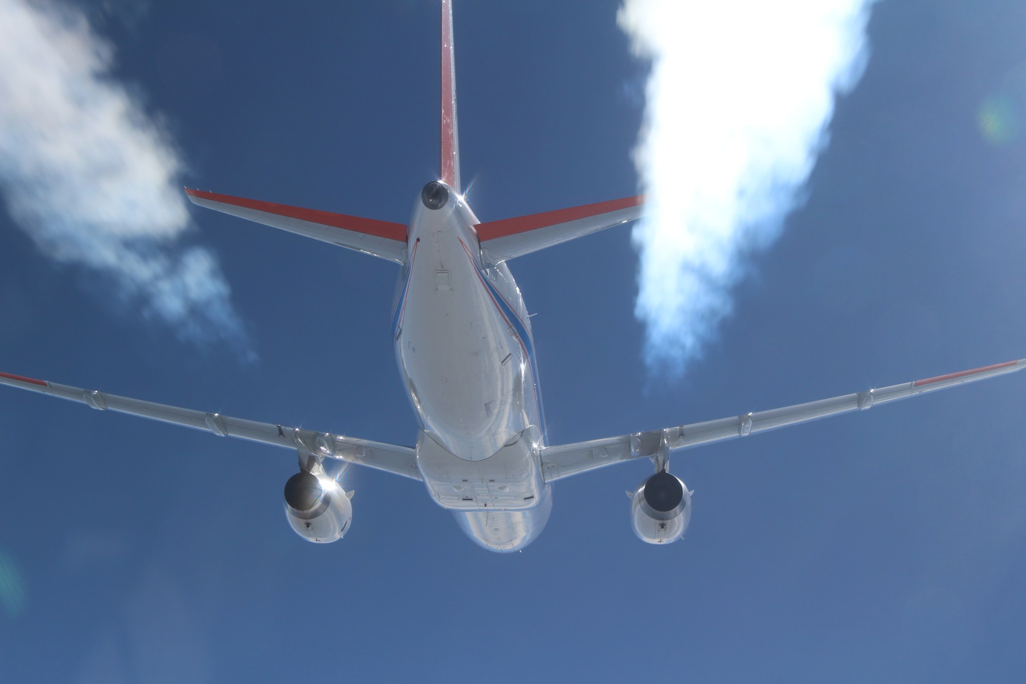 View of an airplane in flight against blue clouds showing contrails.