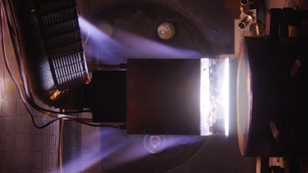 An object mounted on a metal arm is held in a glowing flow of heated gas
