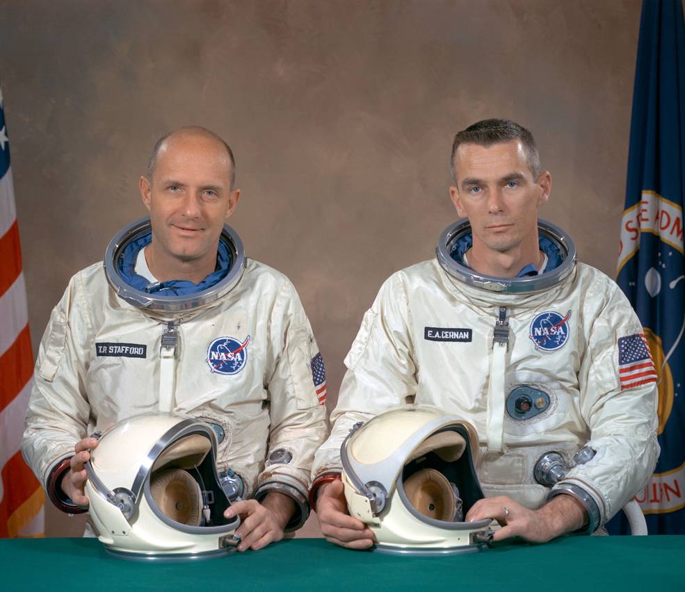 Two men of Gemini crew pose for portrait in white spacesuits in front of flags