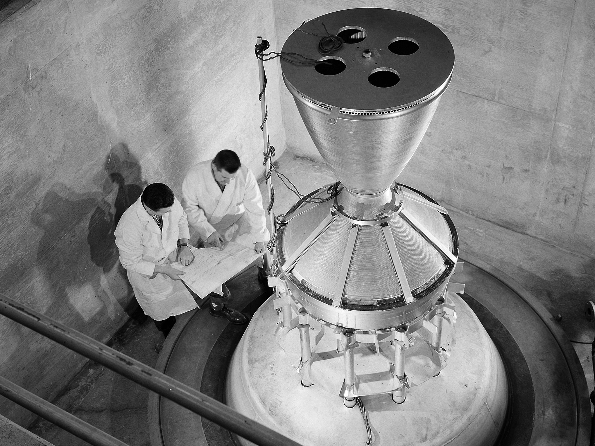 Two engineers in lab coats reviewing test results next to a large engine.