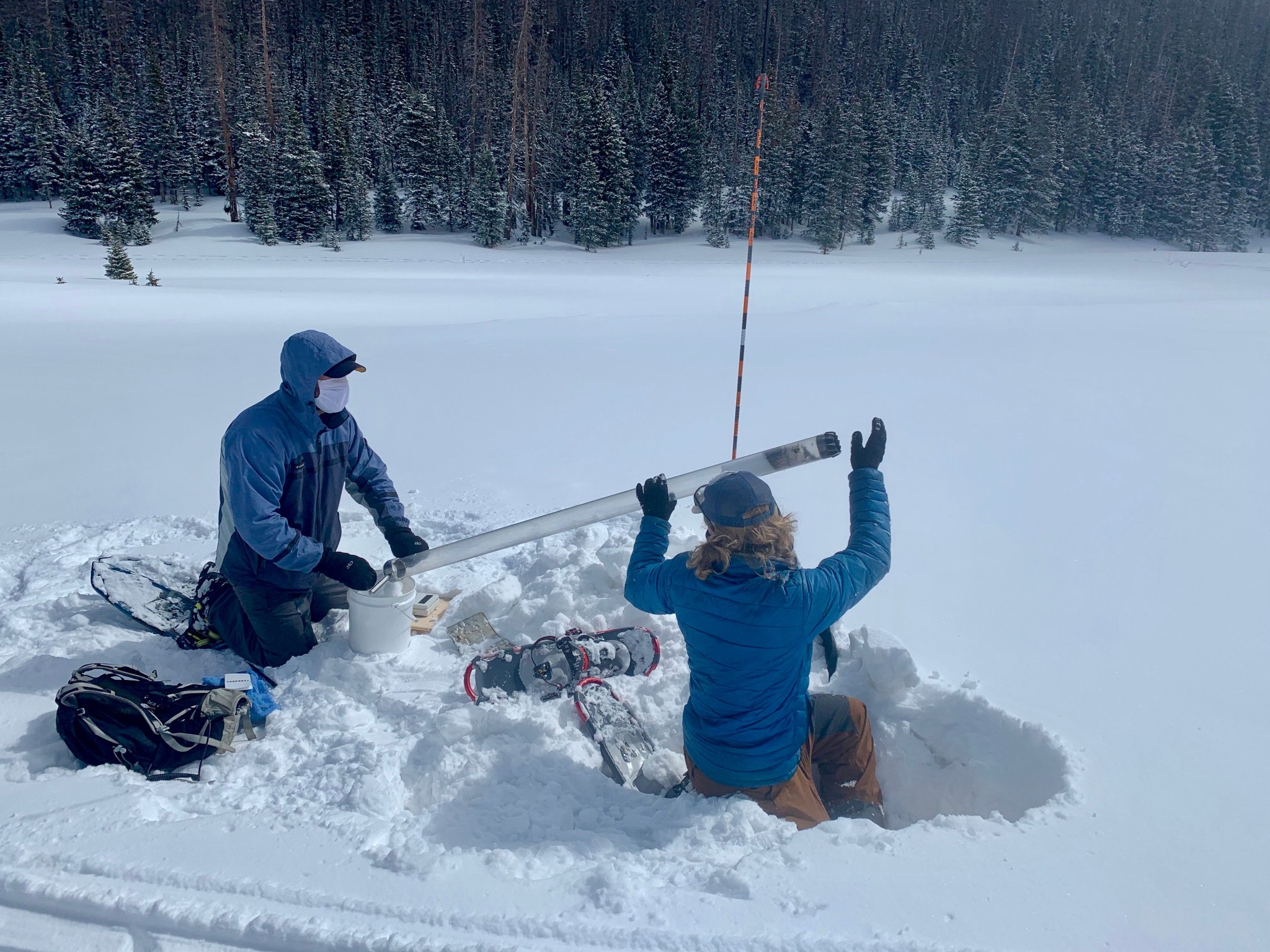 Two graduate students in parkas and snowshoes collect a snow-water equivalent core sample at a snowy site in Colorado.