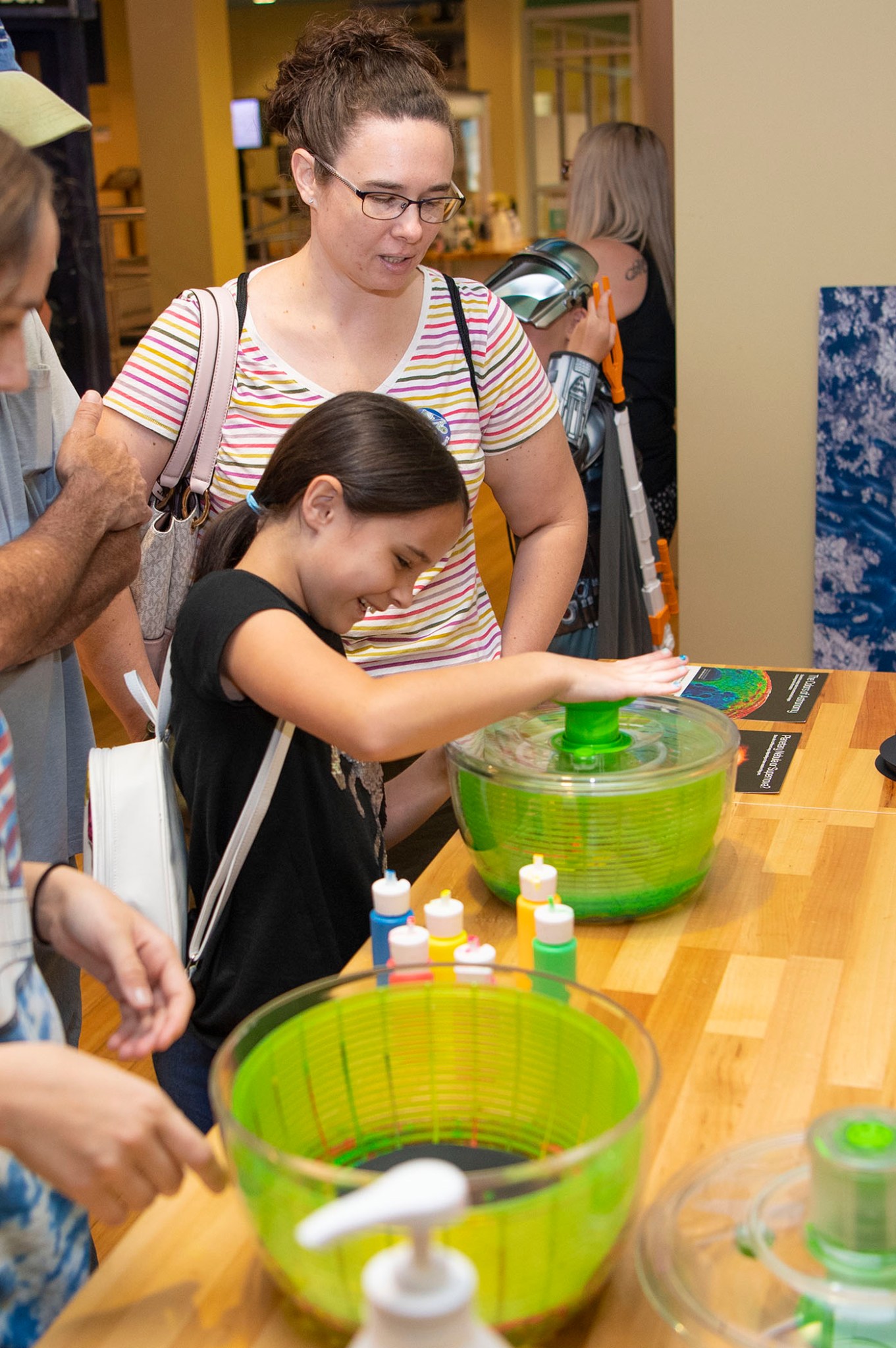 A young girl, watched by her mother, participates in the tie-dye booth at the INFINITY Science Center
