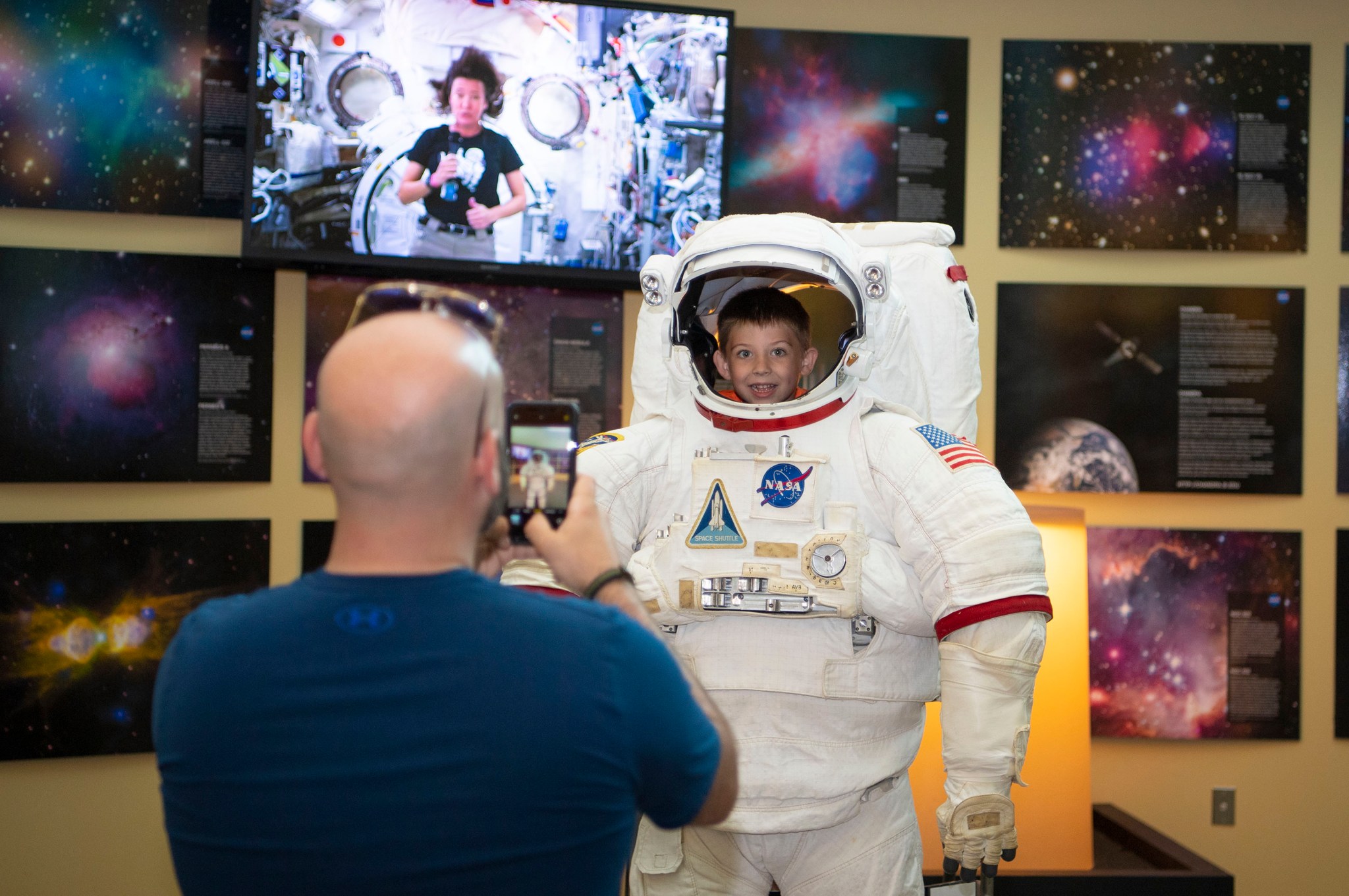 A father takes a picture of his young son posing inside an authentic astronaut suit at the INFINITY Science Center