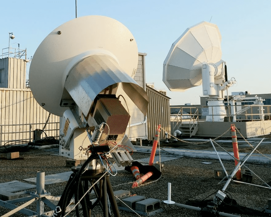 Large satellite dishes positioned on a rooftop and pointed toward a blue sky.