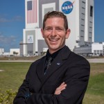 A photograph of Kennedy Space Center's Jesse Berdis with the Vehicle Assembly Building in the background.