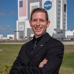A photograph of Kennedy Space Center's Jesse Berdis with the Vehicle Assembly Building in the background.