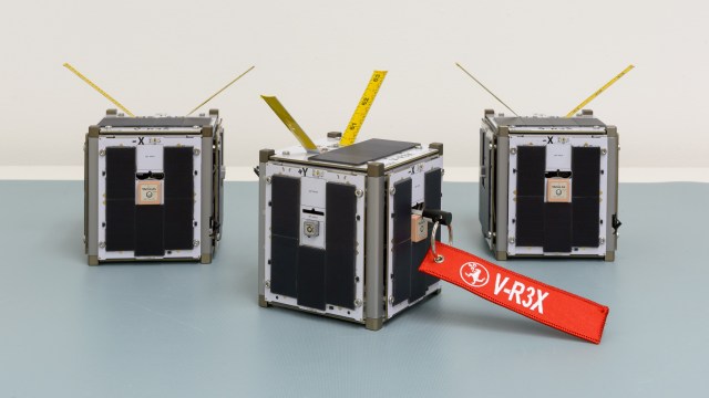 Three small cube-shaped devices on a table, one with a red tag that reads 'V-R3x'.