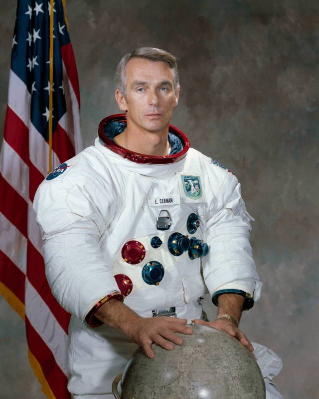 Eugene A. Cernan in white spacesuit posing in front of American flag